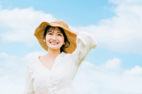 青空で麦わら帽をかぶって笑顔の女性
